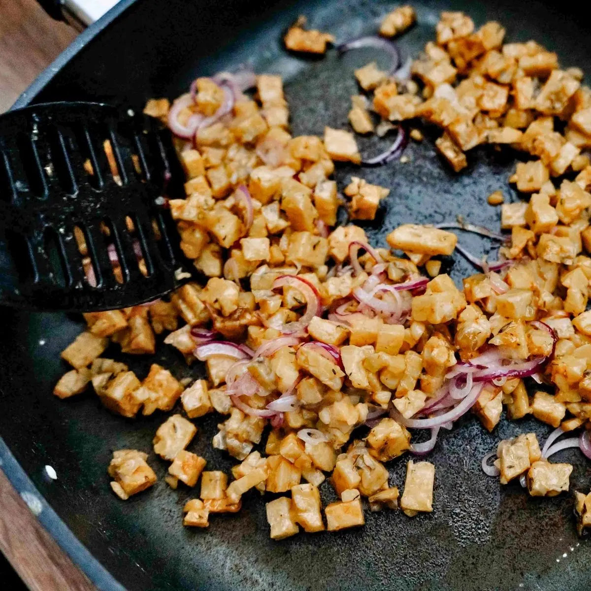 Würfel von Bio Kichererbse-Quinoa-Tempeh werden mit Zwiebeln knusprig gebraten.