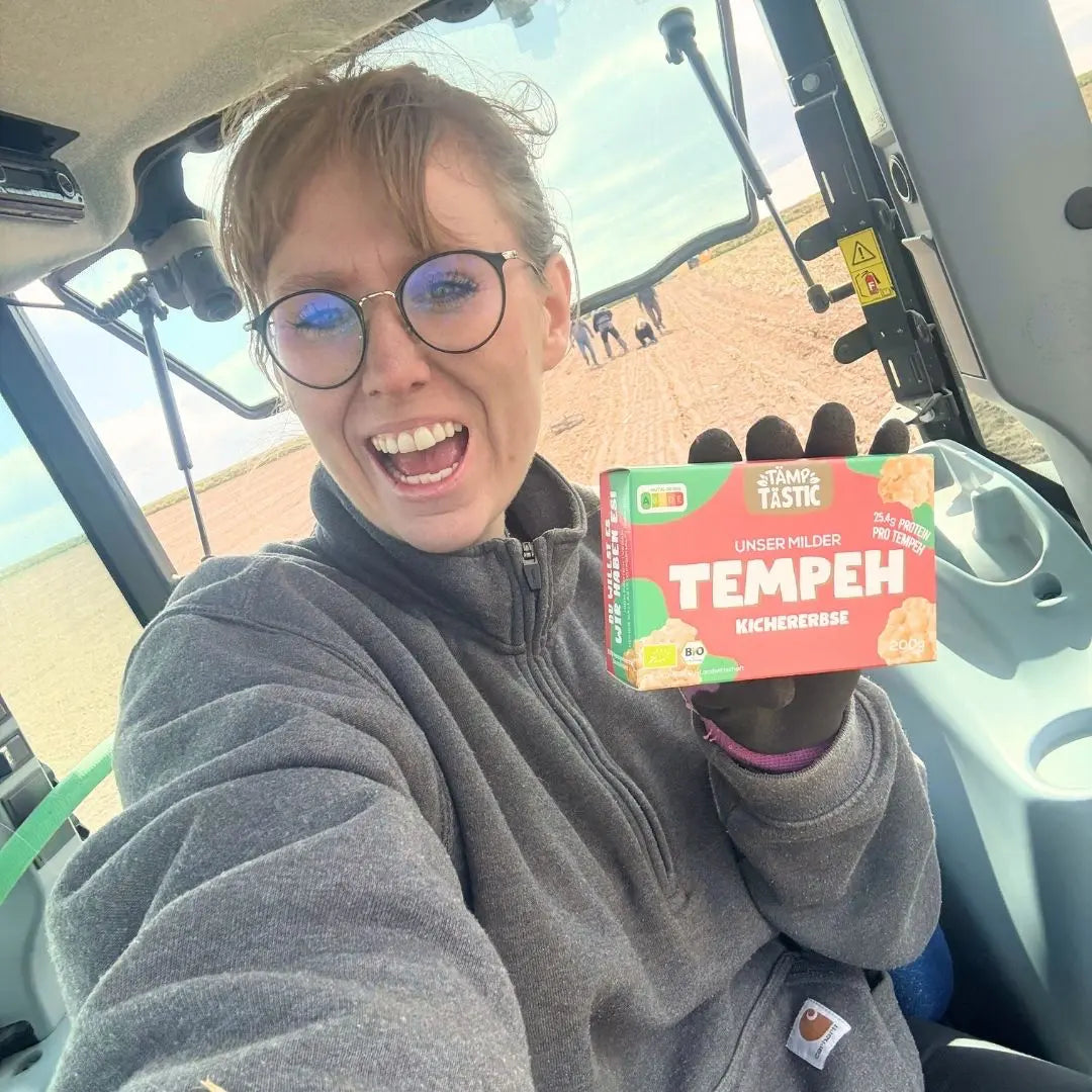 Gründerin Jana auf dem Trecker mit einer Packung TÄMPTÄSTIC Bio Kichererbsen-Tempeh.